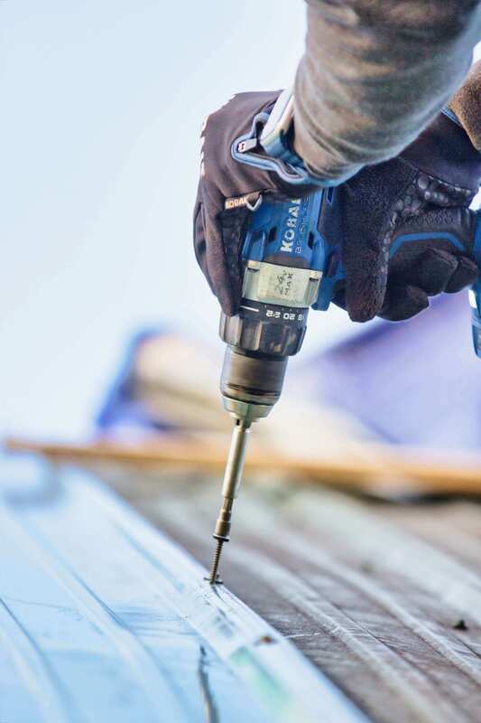 Man installing metal roof with power drill